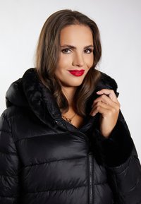 Fekete puffertáska levehető bundás kapucnival, steppelt dizájnnal és cipzáras elülső résszel. Puha, sima tapintású, plüss mandzsettákkal.