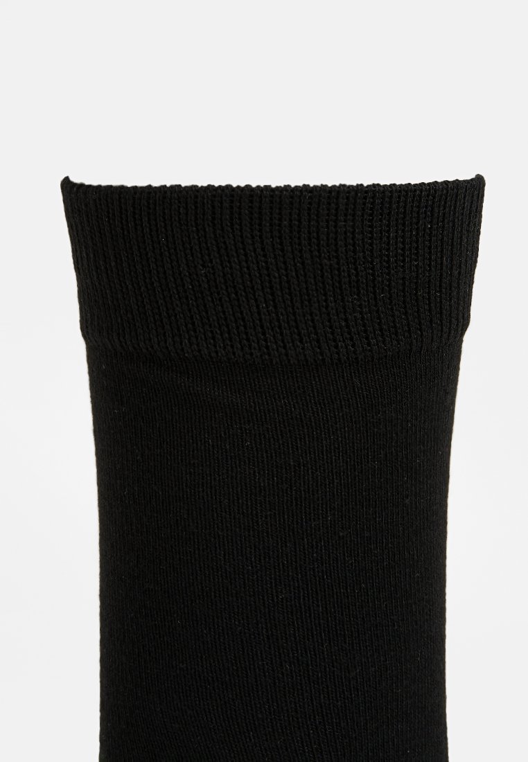 Calcetín negro con un patrón acanalado y un puño seguro. Fabricado en un material suave y elástico, ideal para un ajuste ceñido. Sin logotipos ni diseños visibles.