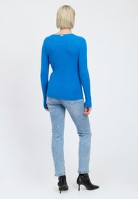 Maglione blu a coste con maniche lunghe, design aderente e scollatura leggermente a barchetta; abbinato a jeans azzurri e stivali neri con tacco alto.
