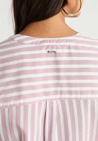 Blusa a righe rosa e bianche, con scollatura rotonda, plissettatura sul retro e un'etichetta argento "Denim" alla scollatura. Tessuto morbido.