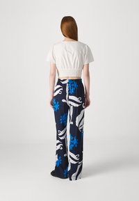 Top curto branco com mangas bufantes; calças largas azul-marinho com grandes padrões florais azuis e brancos, com cintura elástica e corte solto.