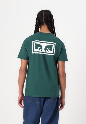 T-shirt de algodão verde com um grande design gráfico branco na parte de trás. Mangas curtas, corte descontraído e decote redondo.