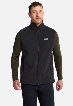Mann mit schwarzer ärmelloser Fleeceweste mit Reißverschluss über einem olivgrünen Langarmshirt, leicht nach rechts gewandt.