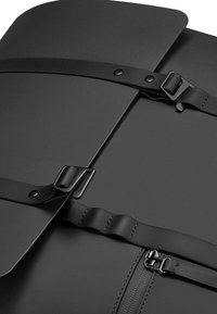 Czarny skórzany plecak z zakrzywioną klapą, regulowanymi paskami i gładką fakturą. Posiada trwałe okucia i minimalistyczny design.