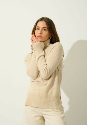 Beige rolák vyrobený z měkkého pleteného materiálu, s ribbed manžetami a lemem, s volným střihem a bočními rozparky.