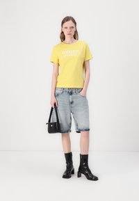Kollane puuvillane T-särk valge "Tommy Jeans" logo ning helesinised teksased lühikesed püksid mustade nahast põlvedeni ulatuvate saapadega. Väike must käsitasku.
