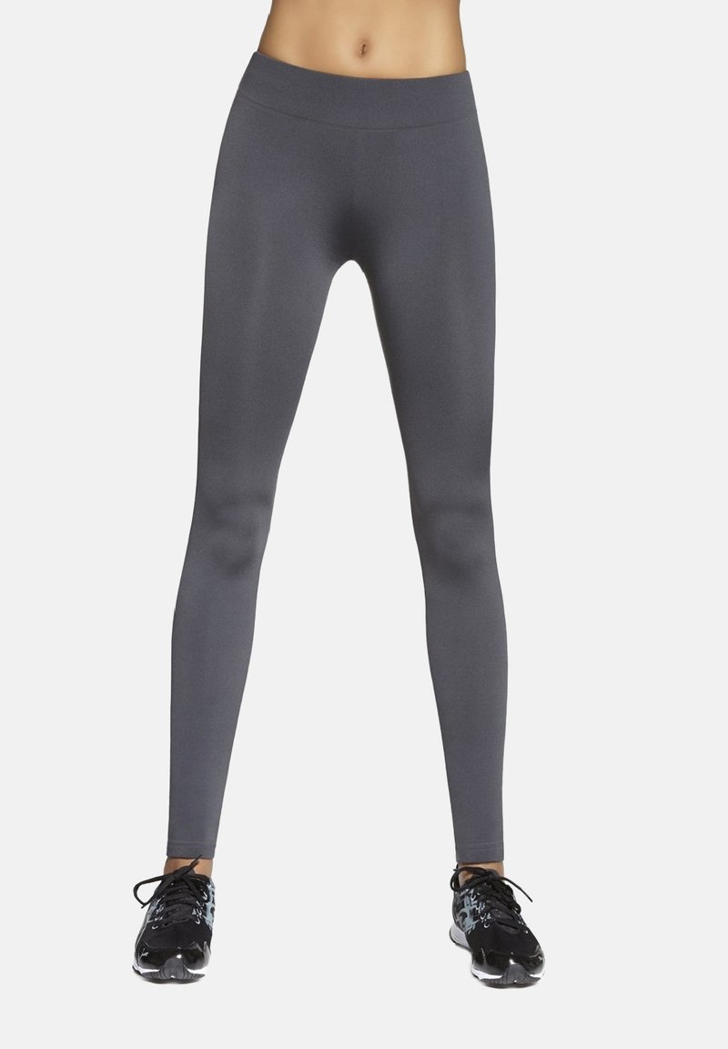 Szare legginsy sportowe z wysokim stanem, o gładkiej fakturze i dopasowanym kroju. Połączone z czarnymi butami sportowymi z wzorzystym akcentem.