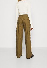 Olivově zelené cargo kalhoty s volným střihem, vybavené několika bočními kapsami a hladkým, odolným materiálem. Nosené s krémovým dlouhým rukávem.