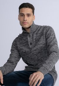 Maglione grigio a maglia con colletto alto e chiusura a tre bottoni, caratterizzato da un motivo testurizzato e polsini a coste.