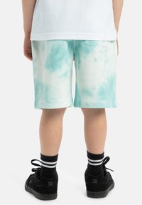 Svetlomodré šortky s tie-dye vzorom z jemného materiálu, s rovnými nohavicami, prehnutým lemom a zadnou vreckom. Kombinované s čiernymi topánkami a pruhovanými ponožkami.