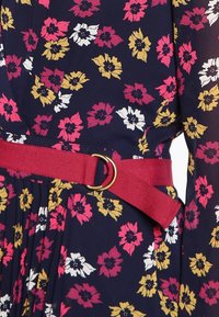 Blumenkleid aus navyfarbigem Stoff mit Mustern in Pink, Weiß und Gelb. Mit einem roten Stoffgürtel mit einer goldenen Ring-Schnalle.