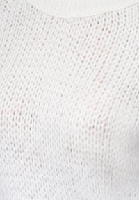 Gruby biały sweter robiony na drutach z teksturowanym wzorem, z prążkowanym dekoltem. Materiał wydaje się miękki i lekko przezroczysty.