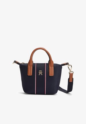 Vojaška torbica iz najlona v mornarsko modri barvi z rjavimi usnjenimi poudarki, opremljena z dvojnimi ročaji, odstranljivim trakom in navpičnimi rdečimi in belimi črtami. Zlati logotip.