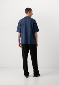 Camisa de manga corta a rayas en azul marino con un corte relajado, combinada con pantalones negros. Presenta un escote redondo y una textura sutil.