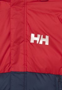 Červená a námořnická izolovaná bunda s prošívanou texturou, na hrudi s výrazným stříbrným logem "HH" a viditelnými stehmi.