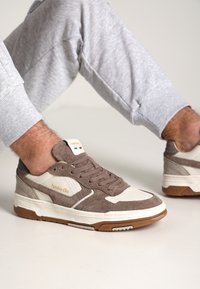 Skrzynkowe sneakersy z zamszu w kolorze brązowym i kremowym o teksturowanym wykończeniu, z białą gumową podeszwą, brązowymi akcentami i złotym logo po boku.