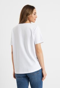 Witte t-shirt met korte mouwen, in een vrij losse pasvorm en met een ronde hals, gecombineerd met blauwe denimjeans. De stof lijkt zacht en glad te zijn.