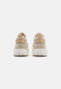 Beige sportcipők texturált anyaggal és velúr részletekkel. Párnázott talppal és kiemelkedő logóval a sarkán.