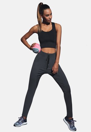 Czarny crop top i ciemnoszare tapered joggery z troczkiem; model trzyma różowo-niebieską piłkę do koszykówki; buty sportowe w kolorowym wzorze.
