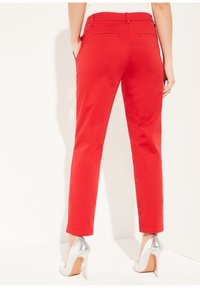 Pantalons tailleur rouges avec une taille mi-haute, poches latérales et poches passepoilées à l'arrière ; assortis à des escarpins argentés brillants.