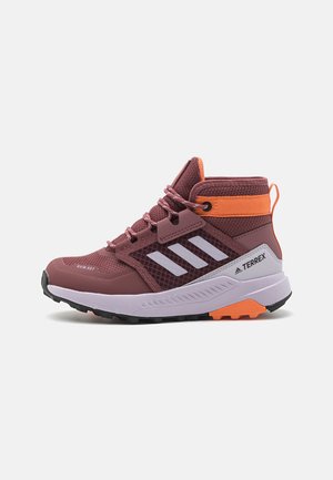 Zapatos de senderismo de caña alta en color marrón burdeos, confeccionados con materiales de malla y goma. Presentan rayas blancas, acentos naranjas y una suela texturada para un mejor agarre.