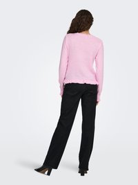 Pink knitted sweater with a ribbed hem, worn with black straight-leg jeans and high-heeled shoes. Hair is curly and falls to the shoulders.
