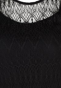 Haut en dentelle noire avec un col rond. Des motifs floraux et géométriques en dentelle intricate recouvrent un tissu noir uni. Texture douce.