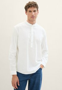 Weißes Langarmhemd mit Stehkragen, Knopfleiste vorne und Knopf an den Bündchen, kombiniert mit blauen Jeans aus Denim. Strukturierter Stoff.