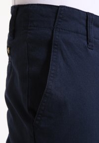 Pantaloni in cotone blu navy con tasche laterali e dettagli di cucitura a vista. Presentano un piccolo etichetta sulla vita. Tessuto morbido.