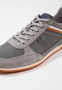 Grå sneaker med en blandning av mocka och texturerad tyg, snören och orange detaljer. Gummisula med ett mönstrat utseende.