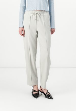Pantalons tapered gris clair avec une taille élastique et un cordon de serrage. Associés à des escarpins kitten heels noirs à bout pointu. Texture lisse.