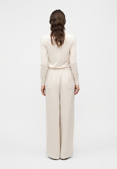 Μπεζ μακρυμάνικη μπλούζα με στρογγυλή λαιμόκοψη και εφαρμοστή γραμμή, σε συνδυασμό με μπεζ παντελόνι φαρδιάς γραμμής με ελαστική μέση και πλαϊνή τσέπη.