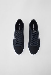 Námořnické plátěné tenisky s bílými gumovými podrážkami, mají kulaté špičky a ploché tkaničky. Branding Jack & Jones viditelný na stélkách.