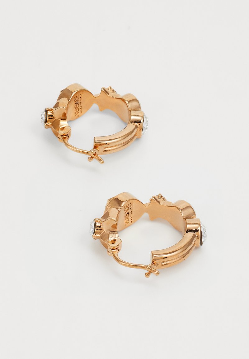 Goldfarbene Creolen mit strukturiertem Design, ausgestattet mit je zwei klaren Strasssteinen. Verschluss an der Unterseite für sicheren Halt.