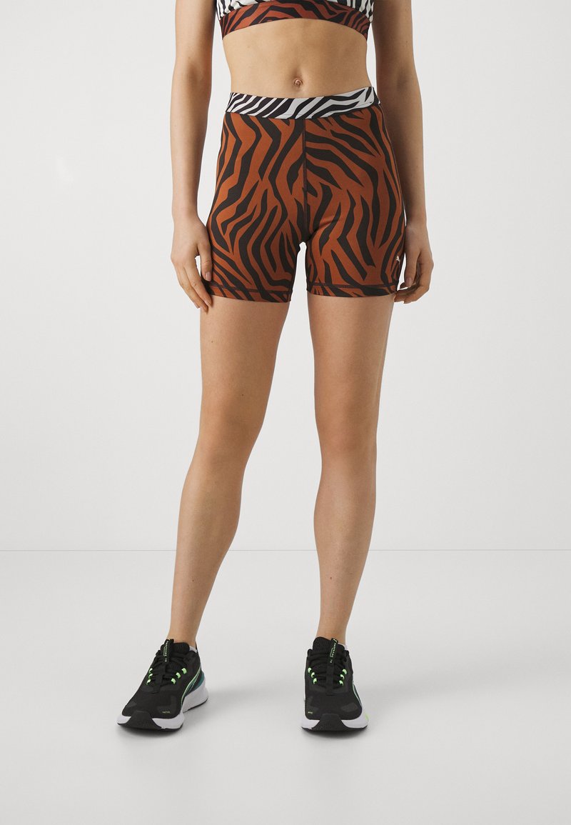 Pantaloni corti a righe zebrate marroni e neri con vita nera uniforme, realizzati in materiale elasticizzato, abbinati a sneakers nere con accenti verdi.