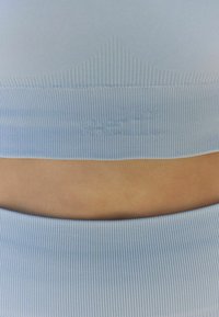 Heled sinine ribiline spordirinnahoidja ümarate kraejoontega. Omab diskreetset logo ja siledat tekstuuri, mis on mõeldud mugavuseks ja paindlikkuseks.