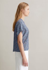 Kortgestructureerde, bloemenpatroon top in het blauw, met een relaxte pasvorm en zacht materiaal, gecombineerd met witte hoge taille broek.