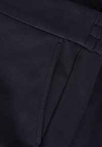 Tessuto blu navy con texture liscia, design sartoriale e cuciture precise, e un dettaglio della tasca visibile sul lato sinistro.