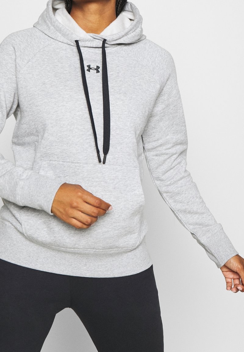 Sweat à capuche gris avec une poche avant, capuche à cordon de serrage et logo noir. Tissu texturé, design décontracté, assorti à des leggings foncés.