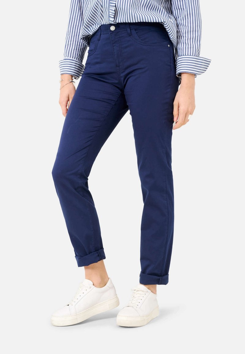 Granatowe bawełniane spodnie o dopasowanym kroju, z podwiniętymi mankietami i kieszeniami z przodu, w zestawie z białymi trampkami. U góry widoczna paskowana bluzka.