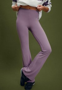 Lila široke leggins hlače iz raztegljive tkanine, z brezšivnim dizajnom in kontrastnim šivanjem, v kombinaciji s črnimi supergami.