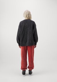 Schwarzes, übergroßes Sweatshirt mit strukturiertem Finish, kombiniert mit lockeren, roten Jogginghosen mit gerafften Bündchen und schwarzen Sneakers.