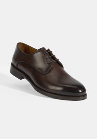 Chaussure habillée en cuir marron avec un bout rond, un laçage, une texture lisse et un petit talon en bois. Style minimaliste sans motifs visibles.