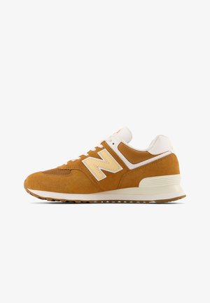 Baskets en daim marron avec des accents blancs, bout arrondi, design à lacets et un grand logo crème sur le côté. Partie supérieure texturée et semelle en caoutchouc.