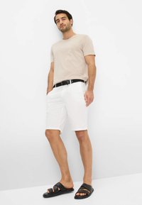 Beige cotton t-shirt, white shorts with pockets, black belt, and black slide sandals. Simple design, relaxed fit, smooth texture.
