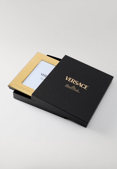 Melna taisnstūra kaste ar zelta burtiem, kurā ir zelta rāmītis fotoattēlu turētājam ar reljefa rakstu un balto ieliktnī.