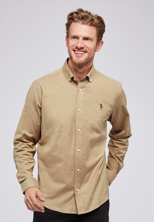 Khaki-pain button-up paita valmistettu puuvillasekoitekankaasta. Siinä on terävä kaulus, pitkät hihat ja pieni kirjailt/logon rintaosassa.