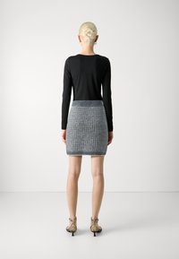 Melnas garās piedurknes blūze, pieguļoša, apvienota ar teksturētu pelēku adītu svārku ar ģeometrisku rakstu un jostu. Uzvilkta ar gaišiem zābakiem.