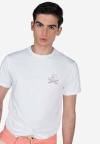 Camiseta de algodón blanca con cuello redondo, que presenta un pequeño gráfico impreso en el pecho en gris y rojo. Tejido suave, ajuste casual.