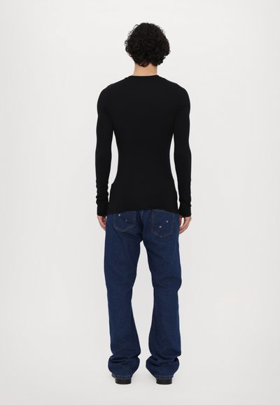 Schwarzes Langarmshirt aus Stretchstoff, kombiniert mit blauen Jeans mit zwei Gesäßtaschen und einer lockeren Passform.